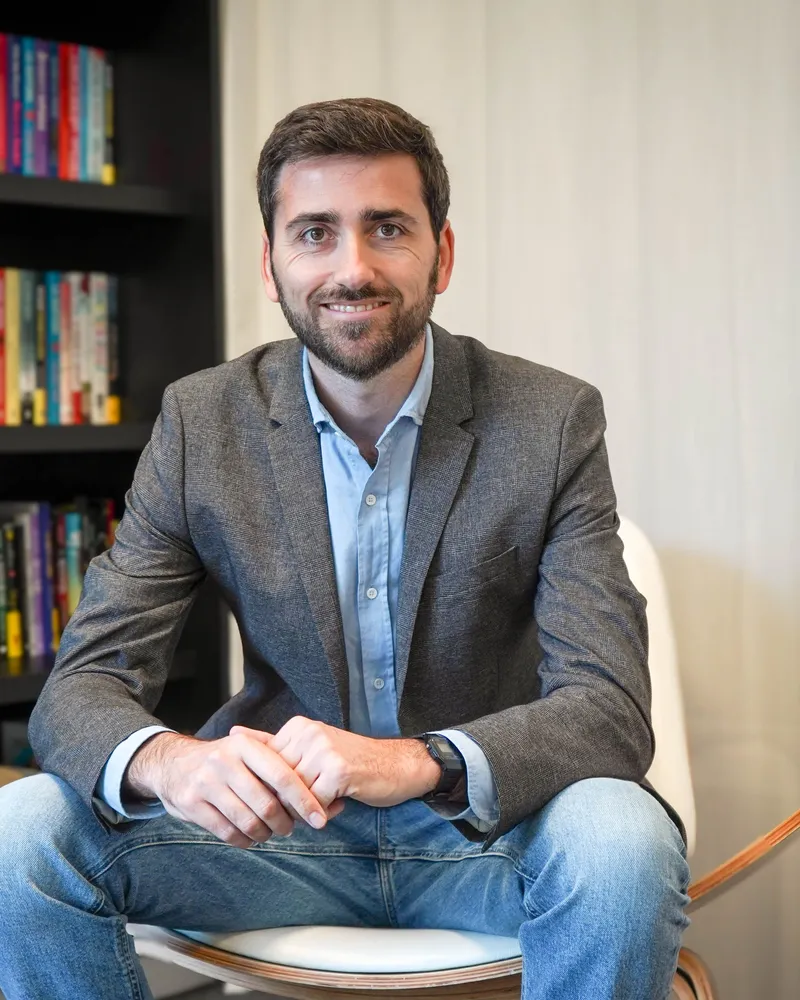El Dr. Borja Quiroga sentado en su consulta, con una biblioteca al fondo
